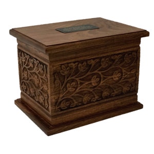May include: A dark brown wooden box with an intricate carved floral design. The box has a flat top with a small brass plaque.