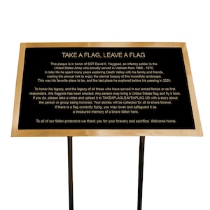 May include: A gold plaque with black lettering on a gold stand. The plaque reads "TAKE A FLAG, LEAVE A FLAG" and honors SGT David K. Haygood, an infantry soldier in the United States Army who served in Vietnam from 1968-1970. The plaque encourages visitors to bring a United States flag and fly it here in honor of those who have served in the armed forces or as first responders.