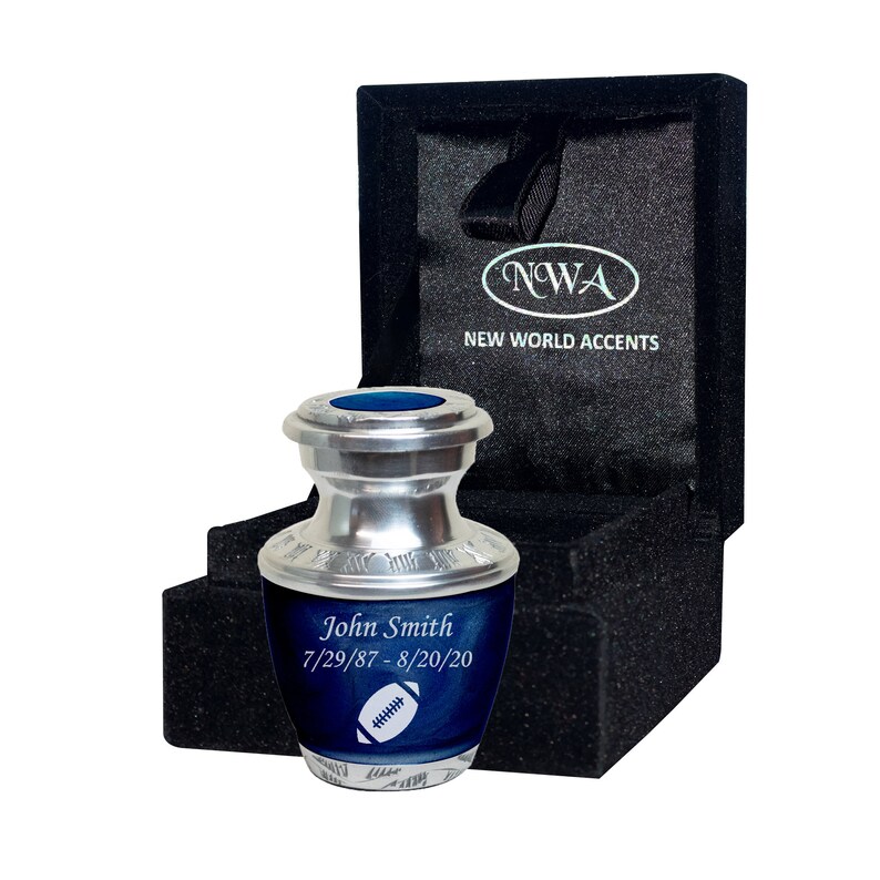 May include: A silver and blue cremation urn with a football design. The urn is engraved with the name "John Smith" and the dates "7/29/87-8/20/20".