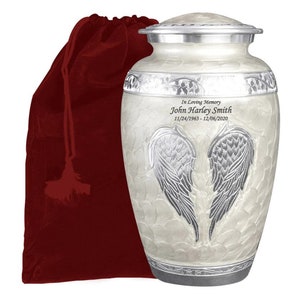 May include: White ceramic urn with silver accents and a pair of angel wings. The urn has a personalized inscription that reads "In Loving Memory John Harley Smith 11/24/1963 - 12/06/2020". The urn is accompanied by a red velvet bag.