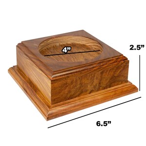 May include: A square, wooden display stand with a circular recessed area. The stand is a warm brown color and measures 6.5 inches long, 4 inches wide, and 2.5 inches high. The edges are slightly rounded, and the wood grain is visible.