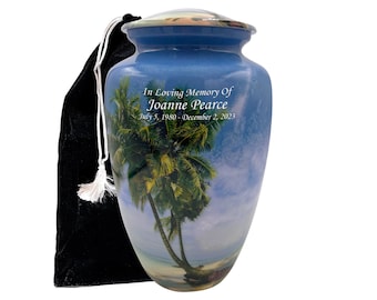 Puede incluir: Una urna de cremación de cerámica azul y blanca con una escena de playa tropical y palmeras. La urna tiene una tapa plateada y está grabada con el texto "In Loving Memory Of Joanne Pearce July 5, 1980 - December 2, 2023".