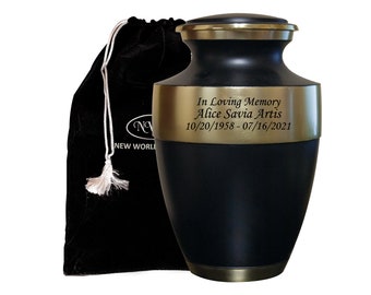 May include: Black and gold metal urn with an engraved inscription: "In Loving Memory Alice Savia Artis 10/20/1958-07/16/2021". The urn is sitting on a black velvet bag with a white drawstring.