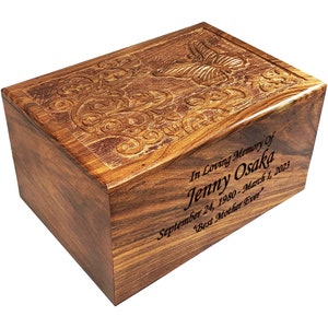 May include: A wooden cremation urn with an engraved butterfly design and the inscription "In Loving Memory Of Jenny Osaka September 24, 1980 - March 1, 2023 'Best Mother Ever'"