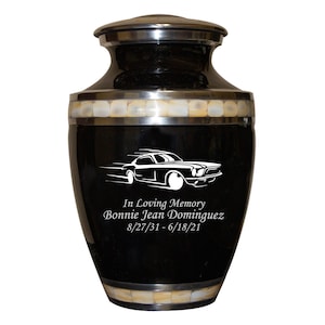 May include: Black cremation urn with a silver lid and a white silhouette of a car with the text "In Loving Memory Bonnie Jean Dominguez 8/27/31 - 6/18/21"