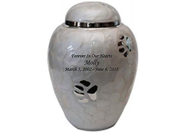 May include: White ceramic pet urn with a silver lid and paw print design. The urn is engraved with the text "Forever In Our Hearts Molly March 5, 2002 - June 6, 2018".