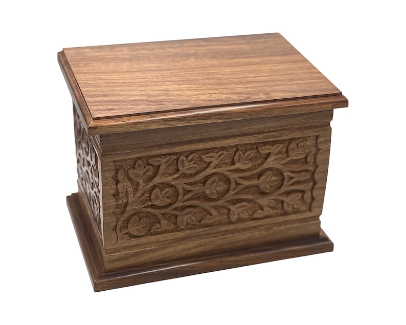 May include: A wooden box with intricate floral carvings on the front and sides. The box is made of dark brown wood and has a smooth, polished finish.