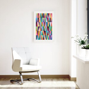 May include: A white armchair with a tufted back and a black metal base sits in a room with white walls and a framed print of a colourful geometric pattern. The print features a variety of triangles in shades of pink, blue, green, yellow, and orange.