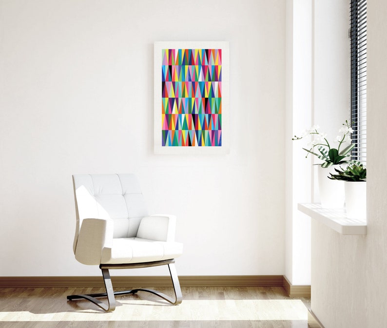 May include: A white armchair with a tufted back and a black metal base sits in a room with white walls and a framed print of a colourful geometric pattern. The print features a variety of triangles in shades of pink, blue, green, yellow, and orange.