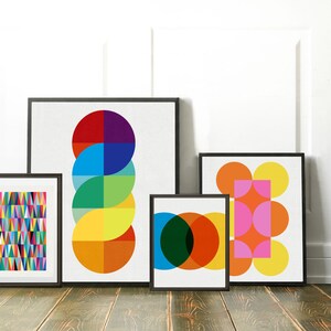 May include: Four framed abstract geometric prints featuring colourful circles, squares, and triangles. The prints are in black frames and are hanging on a white wall.