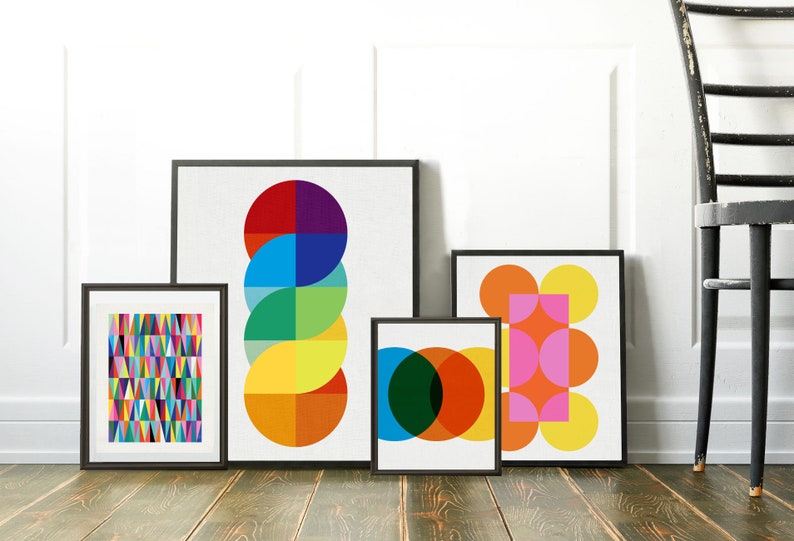 May include: Four framed abstract geometric prints featuring colourful circles, squares, and triangles. The prints are in black frames and are hanging on a white wall.