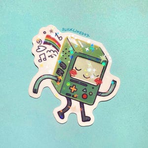 May include: A sticker featuring a green, cartoon-style video game console character with a smiling face, arms, and legs. The sticker has a rainbow, musical notes, and stars. The text "slicklike007" is written on the top.