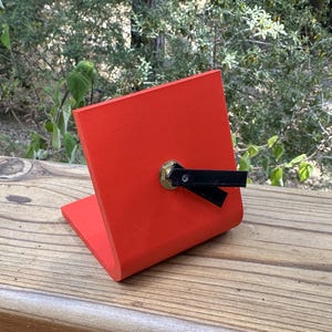 May include: A red, 3D printed phone stand with a black, adjustable arm. The stand is angled to hold a phone upright.