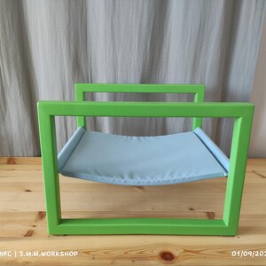 May include: A green metal cat bed with a light blue fabric hammock. The bed is made of a sturdy metal frame and has a comfortable hammock for cats to relax in.