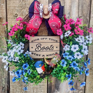 Adorable corona para puerta de entrada con temática de campo y vaquero. Completa con botas de vaquero, flores y un pequeño sombrero de vaquero en la parte superior.