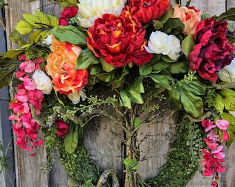 Grote levensboomkrans: oranje, crème en rode pioenrozen en groen deurdecoratie. Boho-decor met mos, bloemen en handgevlochten stam.