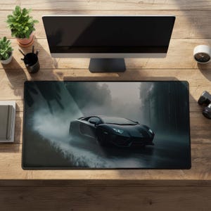 Könnte beinhalten: Eine rechteckige Schreibtischunterlage mit einer kontrastreichen Grafik eines schwarzen Sportwagens, der durch einen nebligen, dunklen Wald fährt. Das Auto ist nach rechts ausgerichtet und seine Scheinwerfer leuchten im Nebel und Schatten der Bäume.
