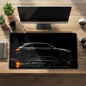 May include: A rectangular desk mat featuring a side profile of a black station wagon car. The vehicle is depicted against a dark background with orange taillights illuminated, reflecting on a wet surface below the car's wheels.