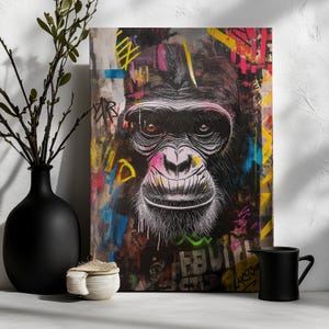 Könnte beinhalten: Leinwanddruck mit dem Gesicht eines Gorillas im Graffiti-Stil. Das Gesicht des Gorillas ist in Schwarz-Weiß gehalten, mit einer rosa Nase und einem lächelnden Ausdruck. Der Hintergrund ist mit farbenfrohen Graffiti-Tags gefüllt.