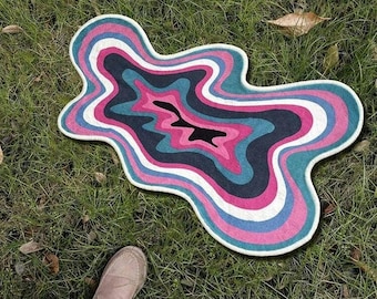 May include: A colorful, abstract rug with a swirling, layered design in shades of pink, blue, and black. The rug has a unique, organic shape and is perfect for adding a touch of whimsy to any room.
