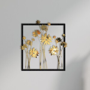 May include: A black framed wall art piece featuring a gold metal floral design. The art is displayed on a white wall between two brown armchairs.