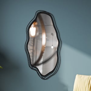 May include: A yellow fabric bench with a black metal frame sits in front of a blue wall with a black, wavy-shaped mirror hanging on it. Two hanging lights with clear glass shades are visible in the background.