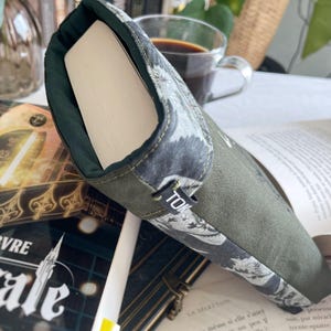 May include: A green book cover with a white and gray floral pattern. The cover has a black label with the word "TOK" on it. The book cover is lying on top of a book with the word "VRE" on the cover.