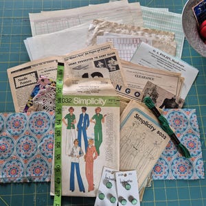 May include: A collection of vintage sewing supplies and ephemera, including Simplicity patterns, fabric scraps with a floral design, buttons, and a measuring tape. The color palette includes shades of blue, green, and cream.