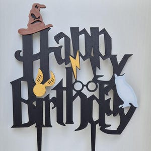 May include: Black cake topper with the words "Happy Birthday" in a Harry Potter font. The topper features a wizard's hat, glasses, a lightning bolt, a golden snitch, and an owl.