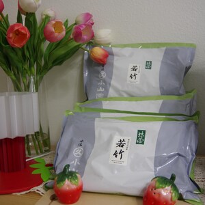 May include: Three packages of food with Japanese text, stacked on a wooden surface. Two ceramic strawberry figurines sit on a wooden cutting board. A vase of tulips in shades of pink, orange, and white is to the left.
