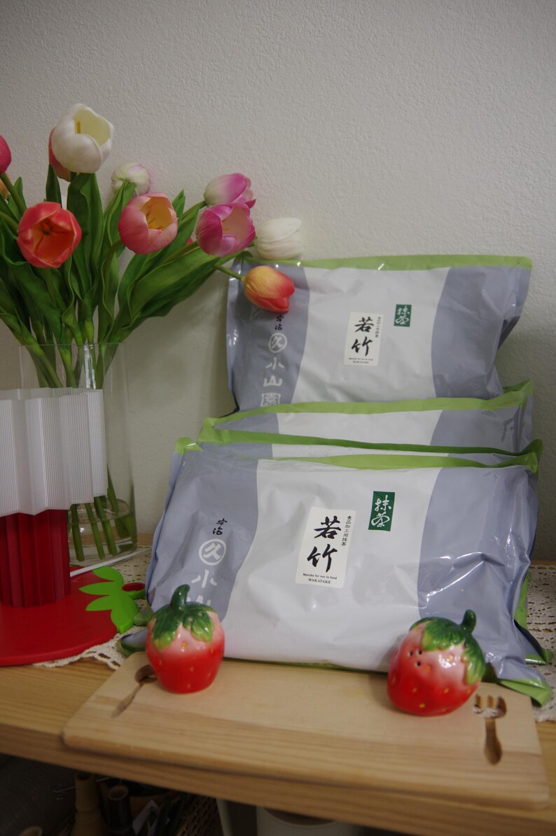 May include: Three packages of food with Japanese text, stacked on a wooden surface. Two ceramic strawberry figurines sit on a wooden cutting board. A vase of tulips in shades of pink, orange, and white is to the left.