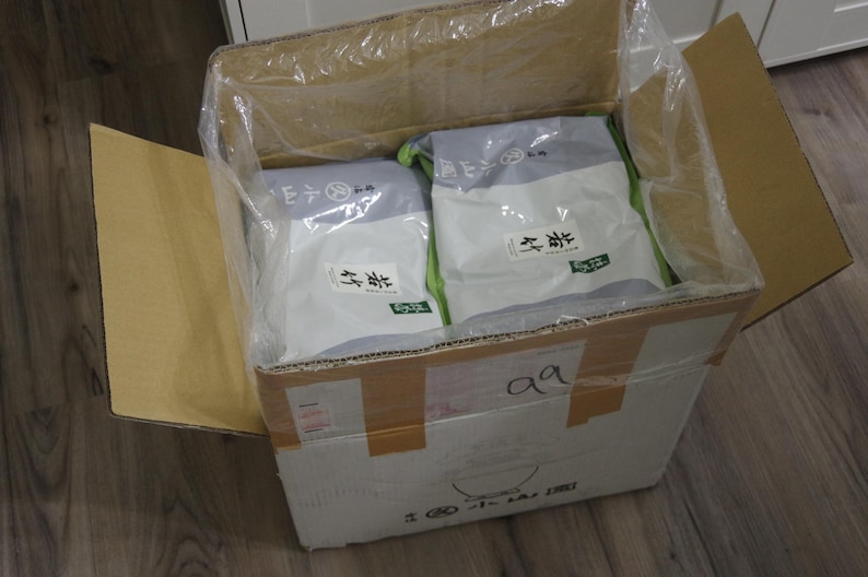 May include: Cardboard box with two packages inside, wrapped in clear plastic. The packages are white and gray with Japanese text and green accents. The box is sealed with tape and has the handwritten letters "aa".