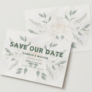 Pode incluir: Cartão de guardar a data com um design floral branco e folhas verdes. O texto diz "Save Our Date" com os nomes "Hannah & William" e a data "Sunday 27th April 2025" e o local "Hockmold Hall".