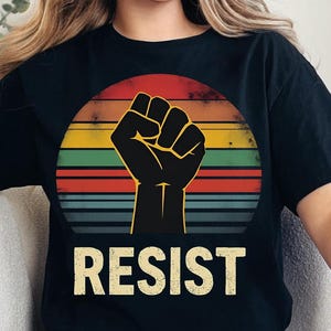 May include: Black t-shirt with a retro-style graphic of a raised fist and the word "RESIST" in yellow.