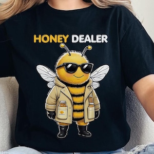 May include: A black t-shirt with the text "Honey Dealer" printed in white. A cartoon bee wearing sunglasses and a brown jacket is holding two bottles of honey.