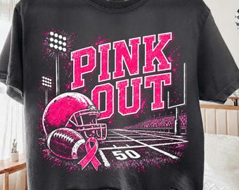 Könnte beinhalten: Ein anthrazitfarbenes T-Shirt mit einem Grafikdruck und dem Text PINK OUT in fetten rosa Buchstaben. Das Design zeigt einen rosa Football-Helm, einen Football, eine rosa Schleife, Flutlichtmasten und ein Football-Feld mit einer 50-Yard-Linie.