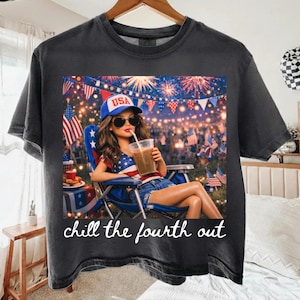 May include: Dark gray t-shirt featuring a graphic of a woman in a USA hat and sunglasses, holding a drink, with fireworks and flags in the background. The text "chill the fourth out" is at the bottom. Patriotic theme.