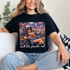 May include: Black t-shirt featuring a graphic of a woman in a patriotic scene, wearing a USA hat and sunglasses, holding a drink. The image includes fireworks and the text "chill the fourth out."