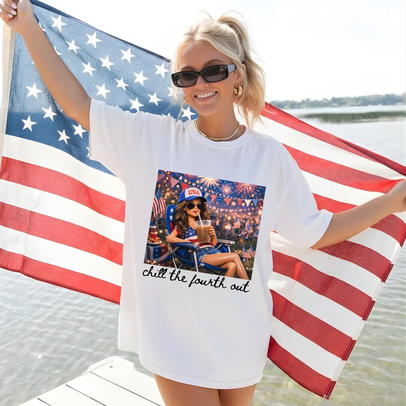 May include: White t-shirt featuring a graphic of a woman relaxing on the Fourth of July, holding a drink. The shirt has the text "chill the fourth out" in a script font. The person is holding an American flag.