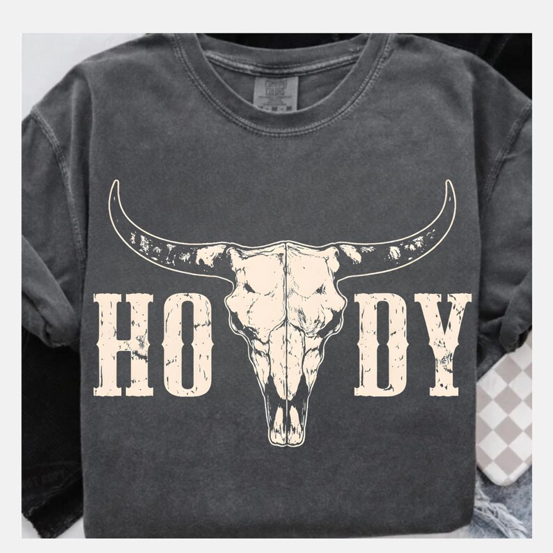 May include: Dark gray t-shirt featuring a white bull skull graphic with the word "HOODY" in a distressed font. The shirt has a crew neck and short sleeves, perfect for casual wear.