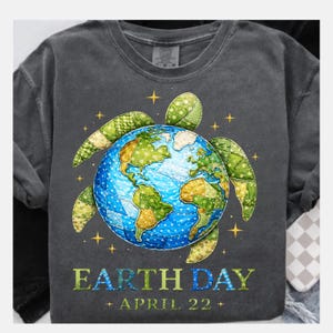 May include: Dark grey t-shirt with an Earth Day design. The graphic shows a globe with patchwork continents, surrounded by a turtle shape. The text "EARTH DAY + APRIL 22 +" is printed below the graphic. The t-shirt is a crew neck.