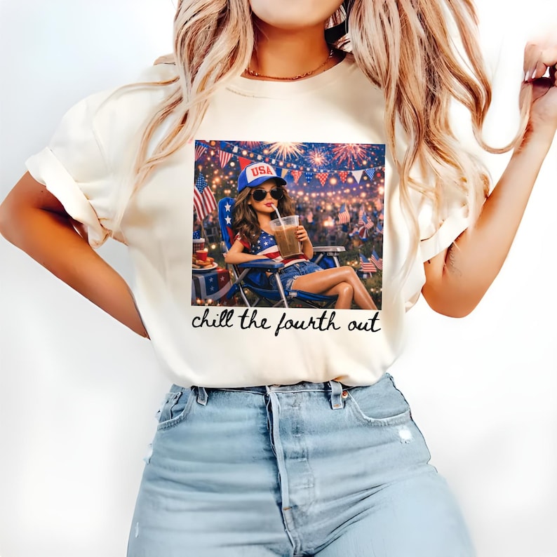 May include: Cream-colored t-shirt featuring a graphic of a woman in sunglasses and a USA hat, enjoying a drink while watching fireworks. The text "chill the fourth out" is printed below the graphic. The woman is sitting in a blue and red chair.