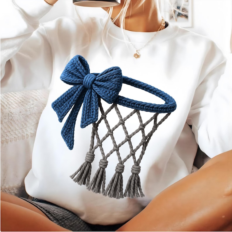 Puede incluir: Sudadera blanca con un lazo de ganchillo azul marino y un dise&ntilde;o de red de baloncesto. La red es gris con tres borlas grises. El dise&ntilde;o est&aacute; centrado en la parte delantera de la sudadera.
