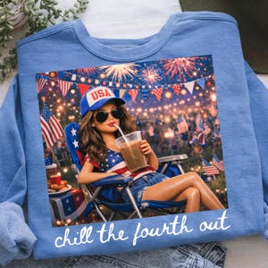 May include: Light blue sweatshirt featuring a graphic of a woman in a patriotic outfit, sunglasses, and a hat that says "USA", holding a drink. The graphic includes fireworks and American flags. The text "chill the fourth out" is at the bottom.