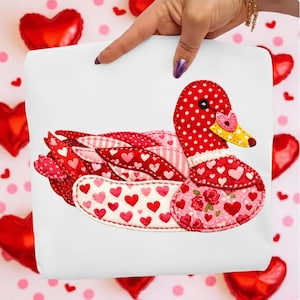 Peut inclure: Un sac fourre-tout blanc avec un motif de canard décoratif. Le canard est fait de tissu rouge, rose et blanc avec des motifs de cœurs et de pois. Le canard a un bec jaune et un accent en forme de cœur.