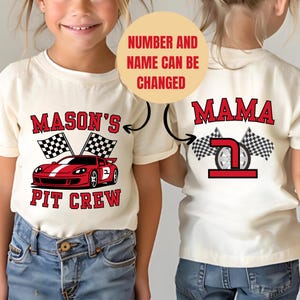Może przedstawiać: Dwie kremowe koszulki z grafiką o tematyce wyścigowej. Jedna koszulka przedstawia czerwony samochód wyścigowy i napis "MASON'S PIT CREW". Druga koszulka mówi "MAMA" z numerem 7 i szachownicami.