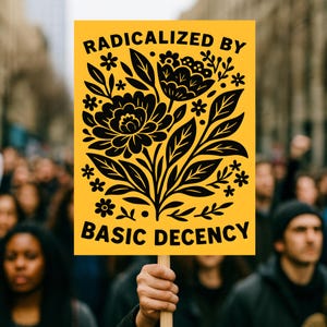 May include: A yellow sign with the words "RADICALIZED BY BASIC DECENCY" in black, with a floral design. The sign is held up in a crowd of people.