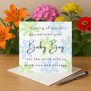 Puede incluir: Una tarjeta de felicitación con el texto "Thinking of you as you welcome your Baby Boy into the world with so much love and courage." La tarjeta está decorada con diseños de flores azules y verdes. Un bolígrafo descansa sobre el sobre.