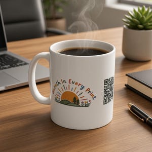 May include: A white ceramic mug filled with a steaming dark beverage. The mug features a colourful graphic of a sun rising over hills with trees and flowers, accompanied by the text Warmth In Every Print and a black and white QR code on the side.