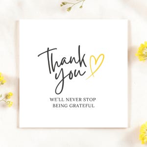 May include: A square white card featuring the black handwritten text Thank you, a yellow hand-drawn heart symbol, and the black printed text WE'LL NEVER STOP BEING GRATEFUL centered below the main greeting.